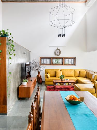 Living room with yellow sectional, wooden console, and geometric pendant under double-height ceiling