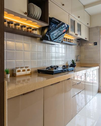 Beige galley kitchen with textured tile backsplash, stone countertop, and glossy cabinetry under warm shelf lighting