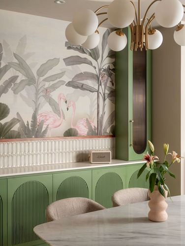 Sage green fluted dining cabinetry beneath a flamingo mural, globe chandelier over marble table