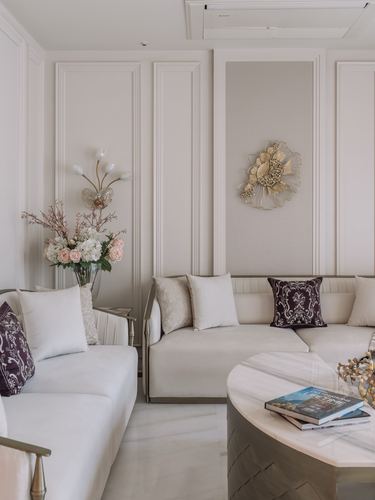 Cream paneled living room with sectional sofa, plum accent pillows, marble coffee table, and gold wall sculpture