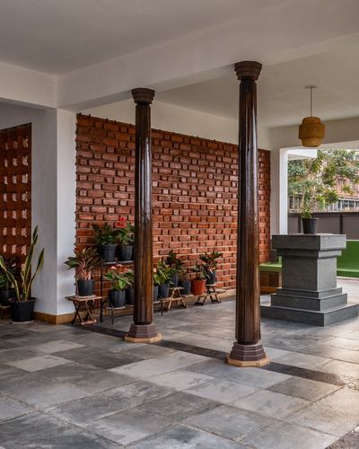 Veranda with dark turned wooden columns, exposed brick wall, potted plants, and stone flooring