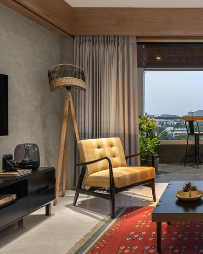 Living room with yellow armchair, tripod lamp, red rug, and balcony view at dusk