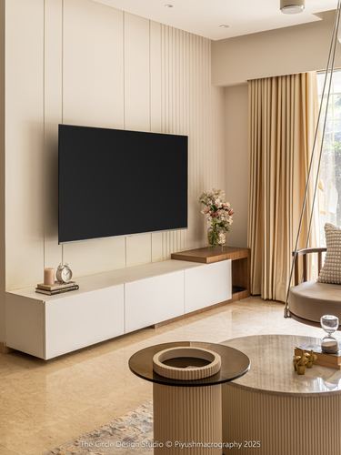 Beige living room with fluted panel tv wall, marble floor, round coffee tables, swing chair by window