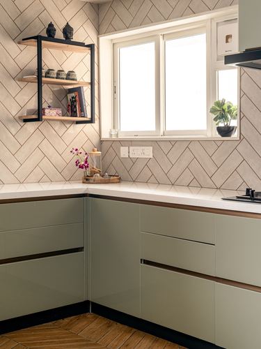 L-shaped kitchen counter with herringbone tile backsplash, sage cabinets, and a black open shelf with decor