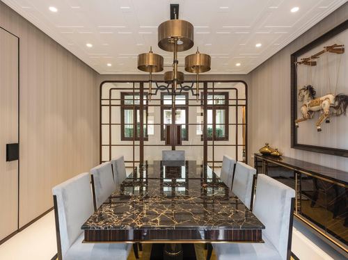 Art deco dining room with brass chandelier, dark marble table, and fretwork screen leading to windows