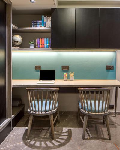 Study nook with two spindle chairs, wall desk, laptop, and teal backlit backsplash under dark cabinets