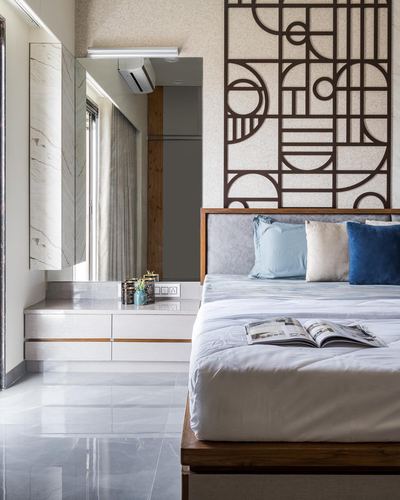 Bedroom with carved geometric wall panel, grey upholstered headboard, blue velvet cushions, marble floor