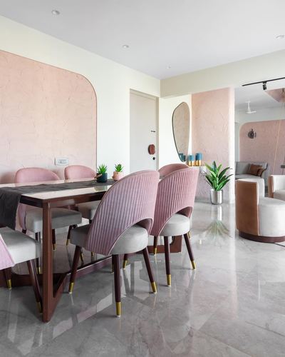 Dining area with pink velvet quilted chairs, wood table, and arched textured pink wall