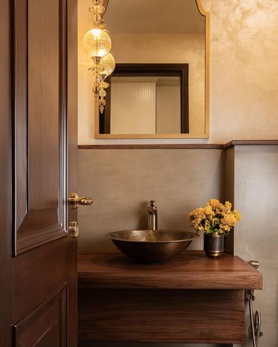 Powder room with hammered metal vessel sink, wood vanity, arched mirror, and open carved wood door