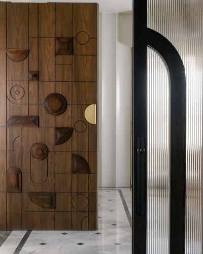 Carved geometric wooden door beside a black-framed arched fluted glass door on marble floor