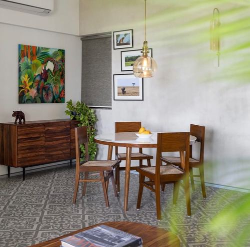 Dining nook with round wood table, cane chairs, patterned floor tiles, and a gallery wall under a globe pendant light