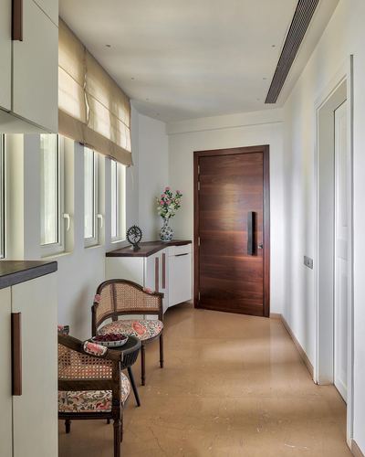 Narrow entrance passage with cane chairs, wooden door, and polished stone floor