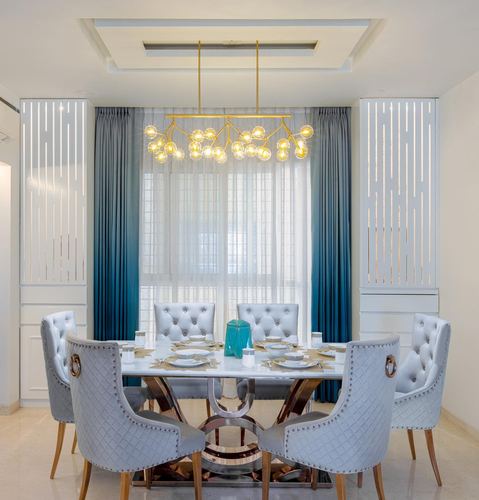 Dining room with marble table, grey tufted chairs, brass branch chandelier and teal ombre curtains