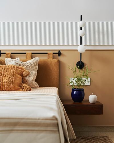 Mustard velvet headboard with cushions beside a floating wood nightstand and globe sconce