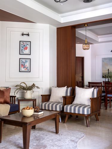 Living room with striped armchairs, wood coffee table, and fluted wood partition to dining area beyond