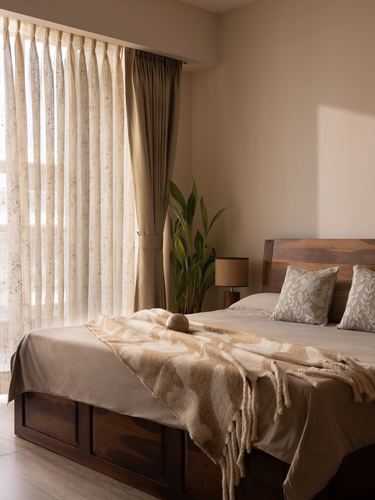 Bedroom with wooden panelled bed, sheer curtains, and textured throw in warm light