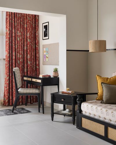 Study nook with black desk and chair beside a cane daybed, floral curtains and pendant light