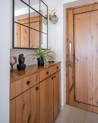 Wooden foyer cabinet with mirror, brass sconce, plant, and paneled wood entry door