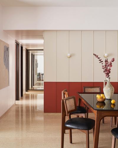 Dining area with cane chairs, glass-top table, and terracotta paneled wall along corridor