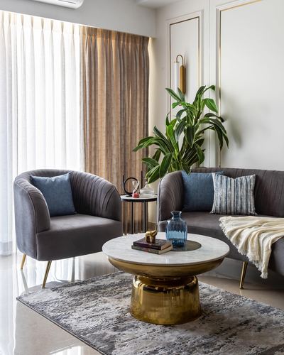 Living room corner with grey channel-tufted sofa, armchair, and round brass-and-marble coffee table