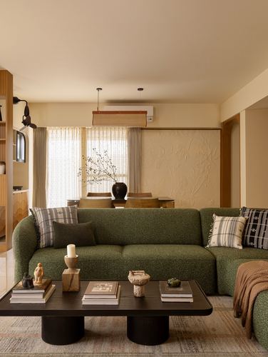 Living room with curved green boucle sofa, dark twin-drum coffee table, and textured plaster wall beyond