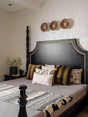 Bedroom with black and gold arched headboard, turned four-poster bed, and three round wooden wall discs above.