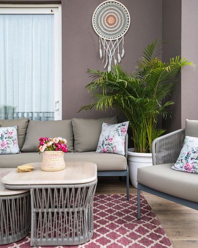 Balcony seating area with grey sofas, floral cushions, rattan tables, and a wall dreamcatcher
