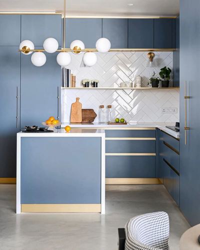 Blue kitchen with white herringbone tile backsplash, brass accents, and a globe pendant light over the island