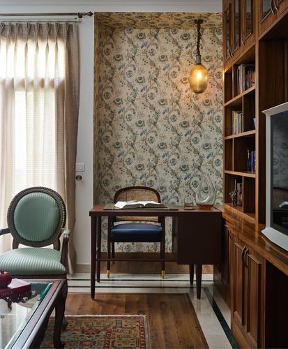 Study nook with floral wallpaper niche, wooden desk, cane chair, and bookshelf in a Delhi home