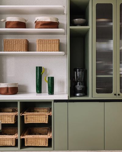 Sage green pantry cabinetry with open shelves holding woven baskets and glass tumblers