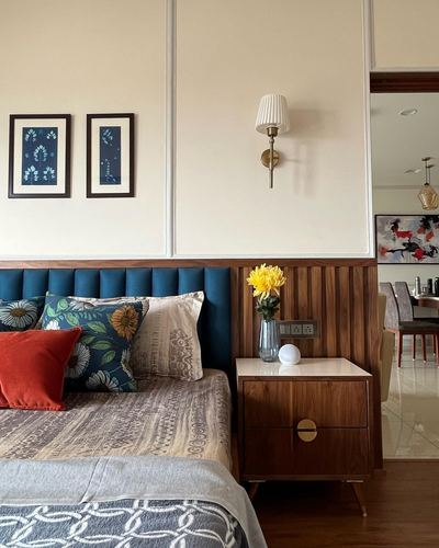 Bedroom with navy tufted headboard, wood-panelled wall, and mid-century nightstand under a brass sconce