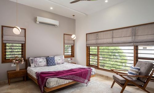Bright bedroom with wooden bed, maroon throw, cane chair and large louvered windows showing greenery