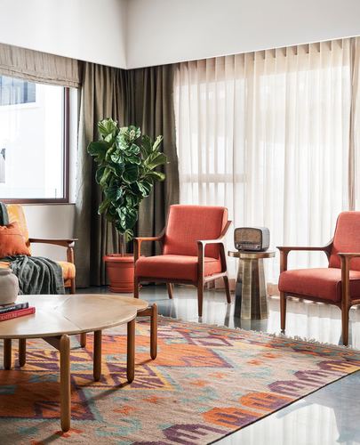 Living room with orange armchairs, kilim rug, fiddle-leaf fig and sheer curtained windows