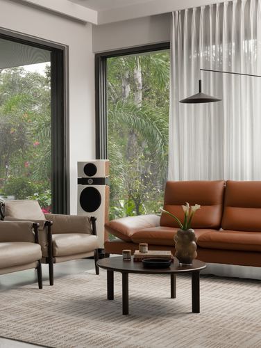 Living room with tan leather sofa, round dark coffee table, and floor-to-ceiling windows facing greenery