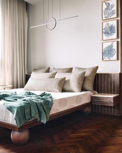 Bedroom with dark wood herringbone floor, bed on sphere legs, green throw and fern prints