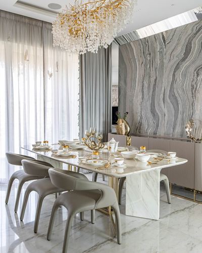 Marble dining table set for a meal beneath an ornate floral chandelier, backed by a veined stone wall
