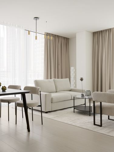 Minimalist living-dining space with beige boucle chairs, glass coffee table, and floor-to-ceiling curtains
