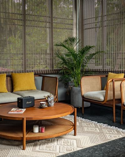 Cane armchairs and round wooden coffee table in tropical living room with woven blinds