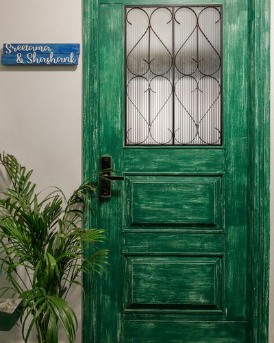 Distressed green wooden entrance door with wrought iron scrollwork grille and nameplate beside it