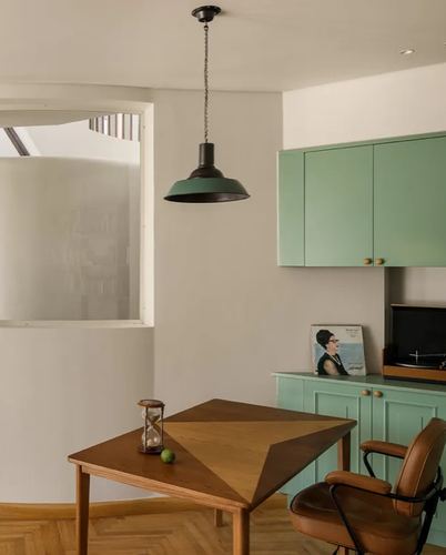 Dining nook with geometric wood table, black pendant light, and sage green kitchen cabinetry