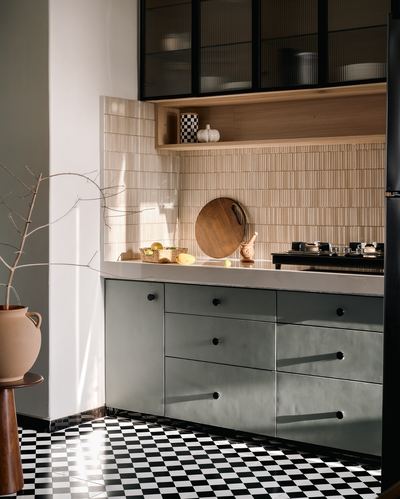 Sunlit kitchen corner with checkered floor, sage cabinets, and ribbed wood backsplash