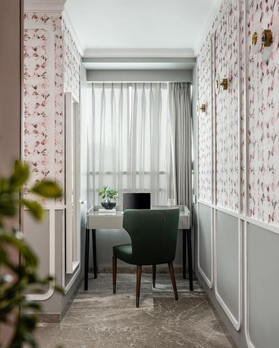 Narrow study nook with floral wallpaper, green velvet chair, desk and sheer curtained window