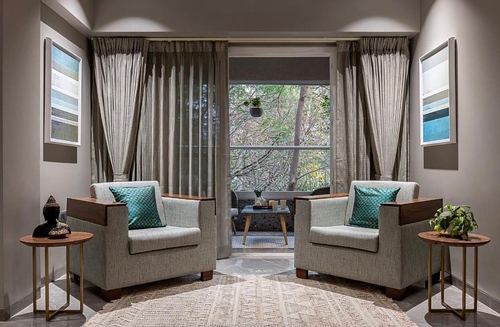 Symmetrical living room with two grey armchairs facing a curtained balcony view in Pune