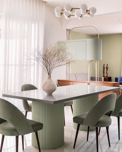 Dining room with marble-top table on fluted green base, sage velvet chairs, and globe chandelier
