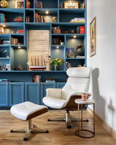 Cream leather recliner and ottoman beside a marble-top table in front of a teal bookshelf wall