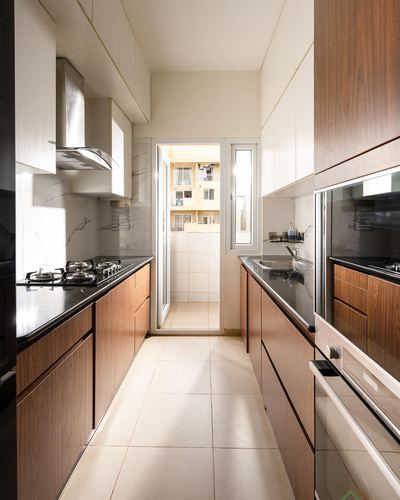 Galley kitchen with wood cabinetry, black countertops, chimney hood, and view through door to balcony