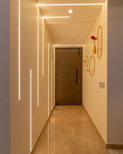 Long hallway with glowing linear ceiling lights leading to a wooden door and gold sconces