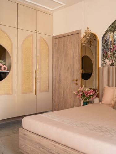 Blush pink bedroom with arched cane wardrobe, wooden door, oval mirror, and star pendant light