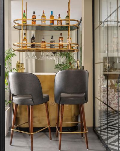 Home bar nook with brass shelving, hanging glassware, and two grey leather barstools