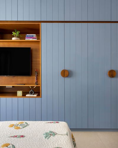 Blue vertical-paneled wardrobe wall with a wood-lined TV niche and round wooden door knobs